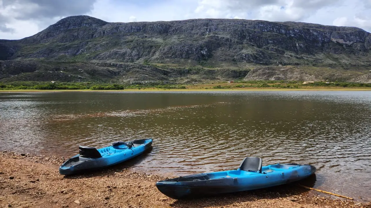 Dois caiaques azuis na margem da lagoa da Lapinha, com a serra ao fundo